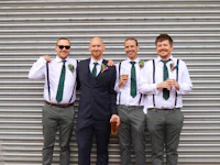a group of groomsmen wearing suspenders and green ties