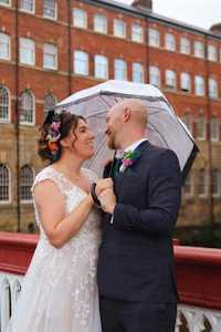 a bride and groom standing under an umbrella on a bridge