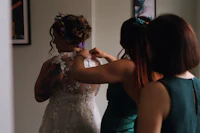 two bridesmaids helping each other with their wedding dresses