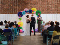 a bride and groom standing in front of a colorful wedding arch