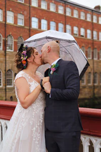 a bride and groom kiss under an umbrella on a bridge